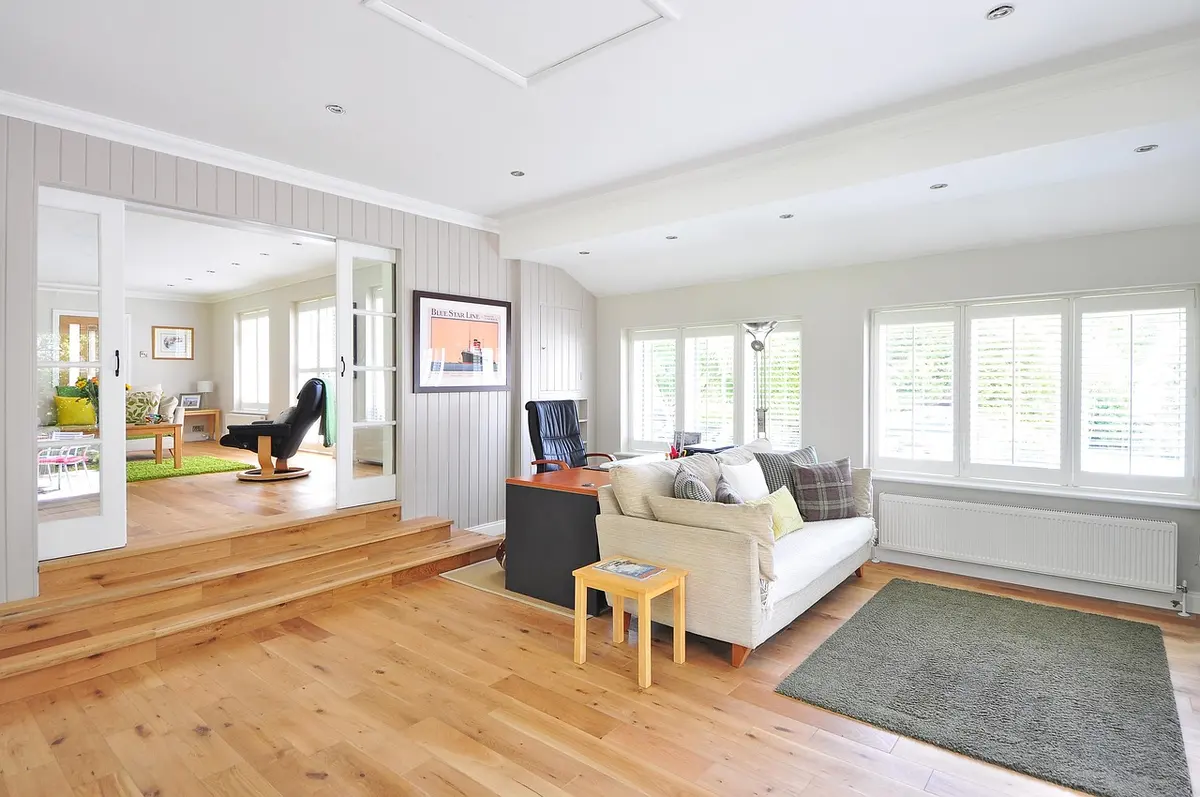 A bright living room with white plantation shutters across a wide bank of windows and a natural oak floor