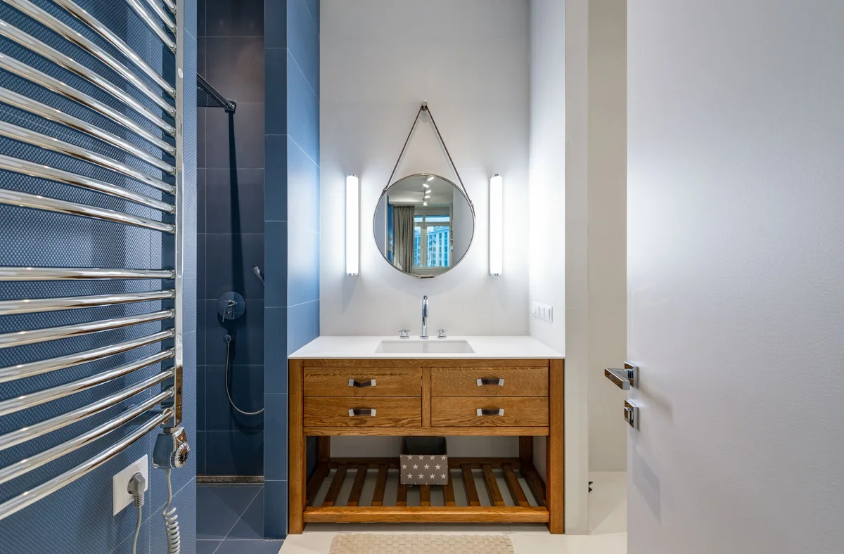 Clean sink placed under round mirror near shower with new flooring