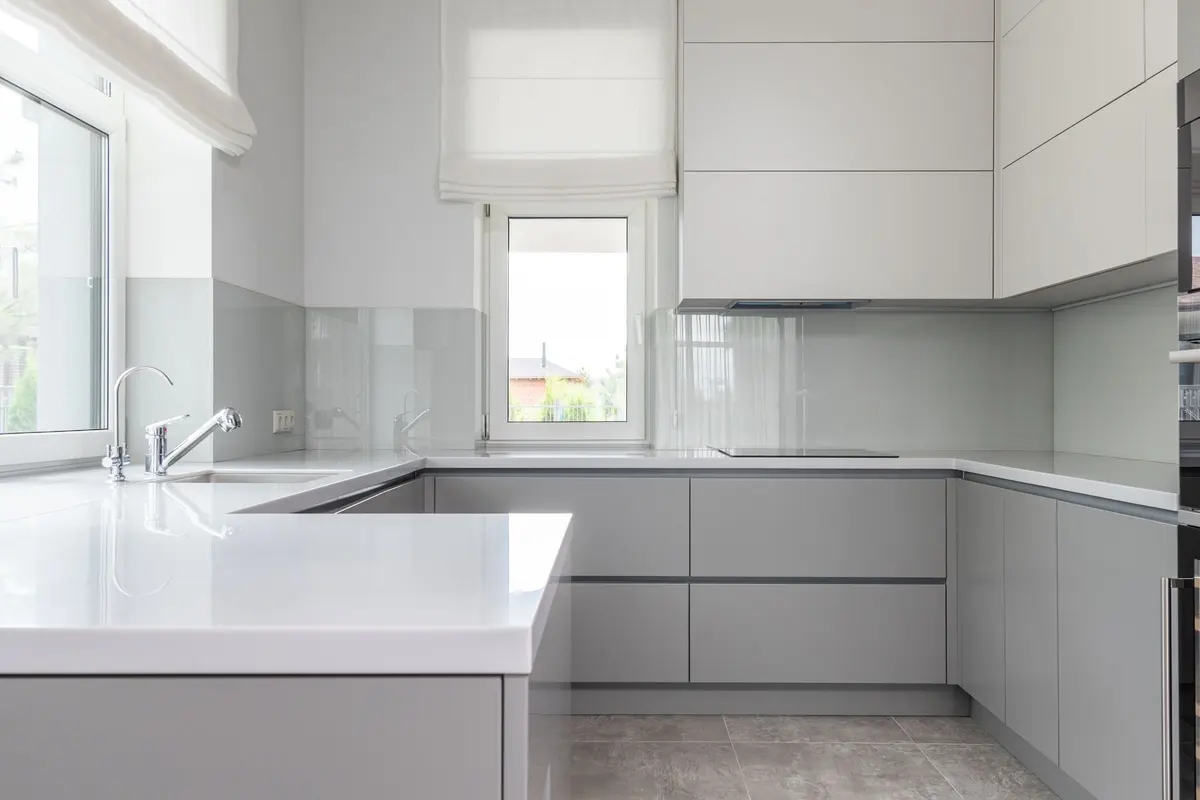 A pale grey kitchen with flat-front cabinets, white countertops and large-format grey tile on the floor
