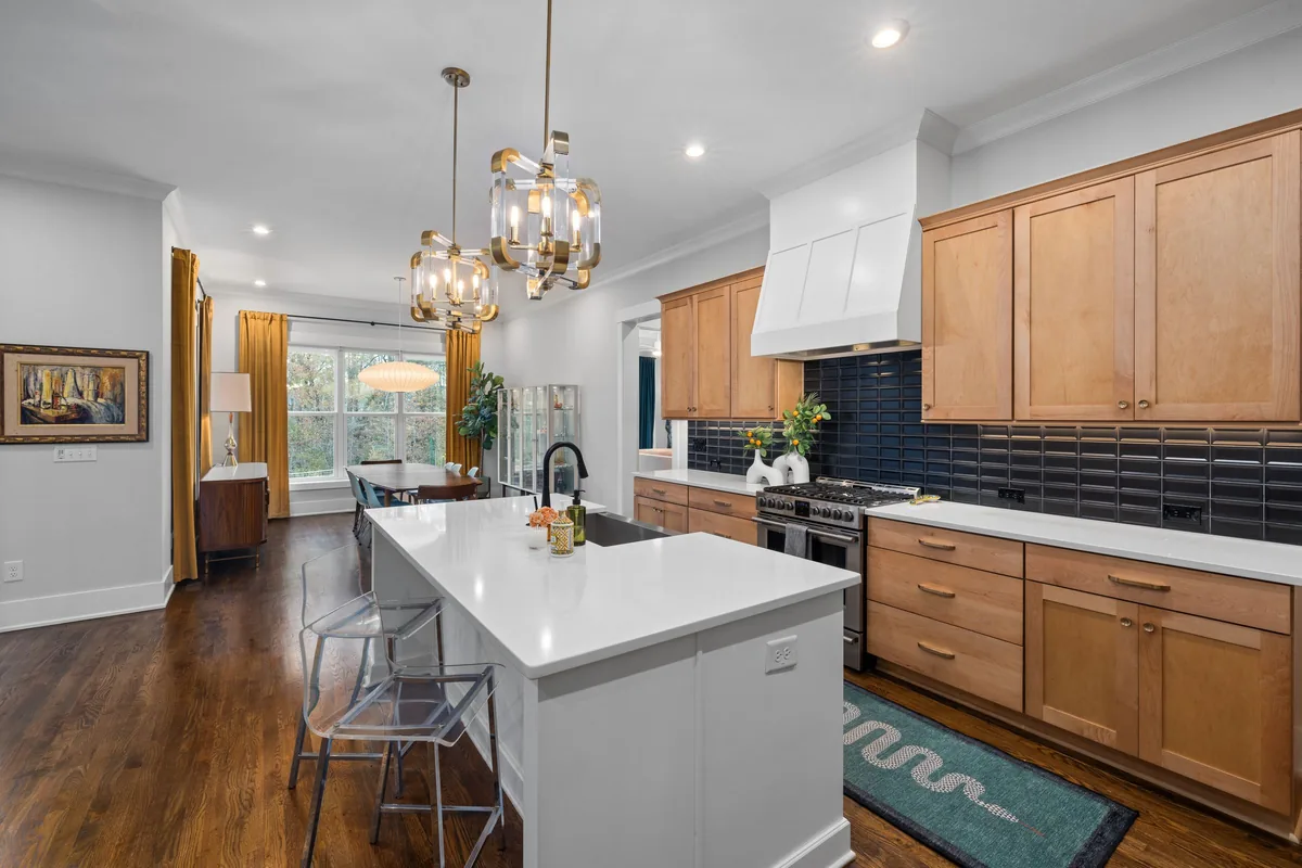 A kitchen with natural wood cabinets, a white island and dark plank flooring running through to the dining area